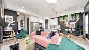 A modern living room with a pink sofa, green chairs, and a kitchen in the background. - Toast & Groove - Sleeps 16 - HTX (Houston)
