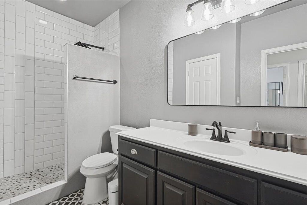A modern bathroom with a walk-in shower, a toilet, a sink with a mirror, and dark cabinets.