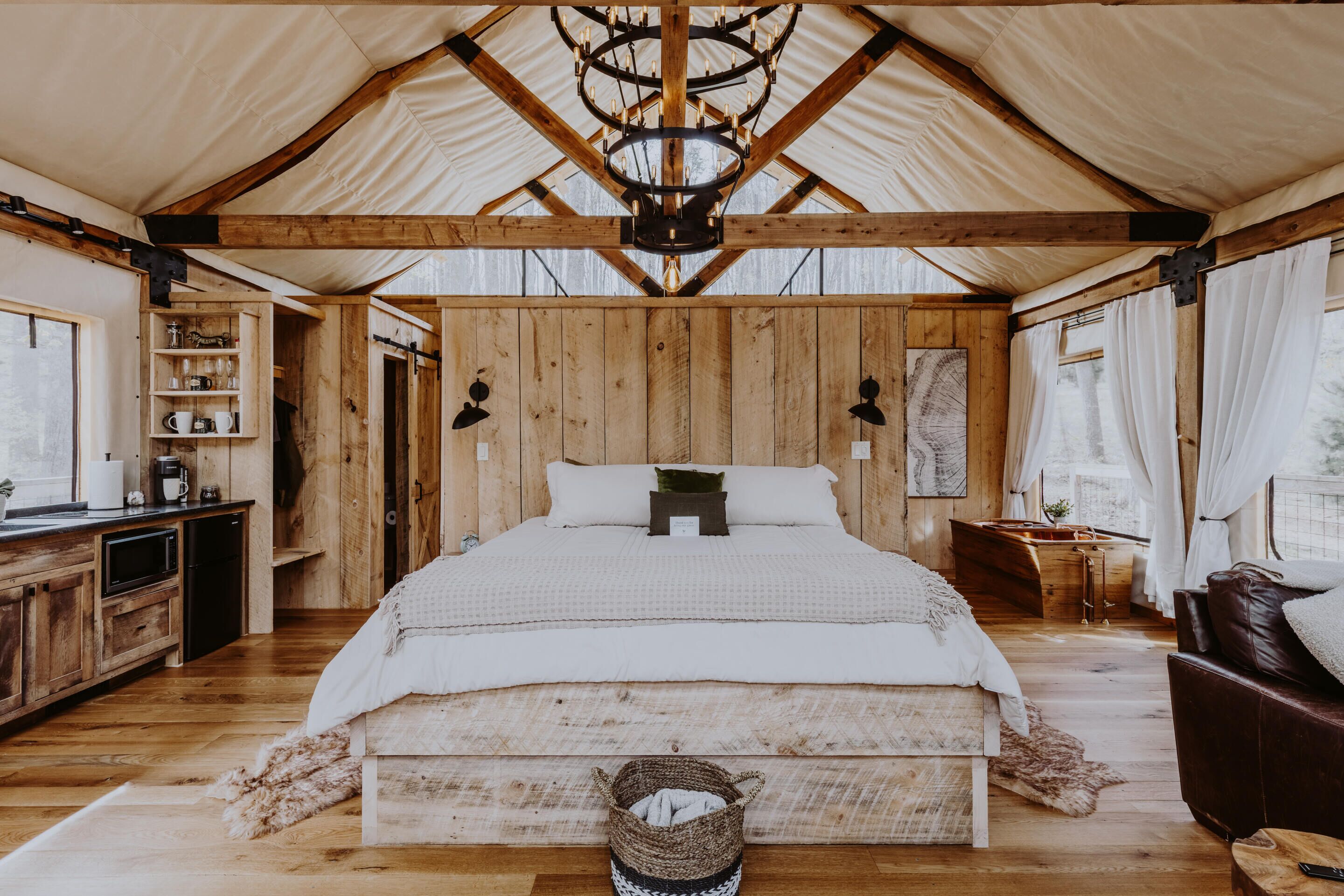 Amplia habitación tipo tienda con una cama grande, paredes de madera, un candelabro y una kitchenette.