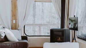 Ein gemütliches Zimmer mit einem Ledersofa, einem weißen Sessel, einem kleinen Holzschemel und einem Fernseher auf einem Schrank.