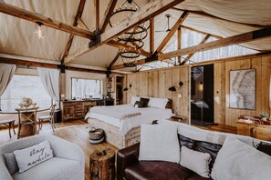 A cozy cabin interior with a large bed, wooden walls, a dining area, and a kitchen.