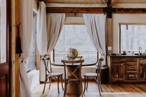 Una mesa de comedor de madera con un globo terráqueo como centro, rodeada de cuatro sillas. Se ve una ventana con cortinas y una zona de cocina parcialmente a la derecha.