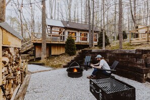 Una cabaña con un brasero y zona de estar al aire libre, rodeada de árboles.