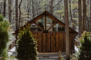 A wooden cabin with a glass front, surrounded by trees.