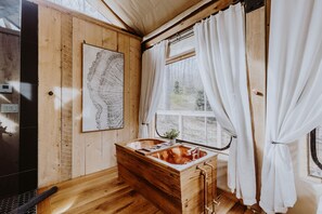 A wooden cabin interior with a wooden bathtub, a window with curtains, and a map on the wall.
