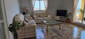 A living room with two sofas, a glass coffee table, a TV, and a potted plant.