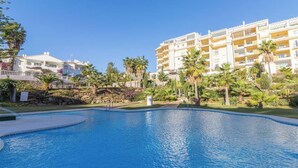 Una piscina rodeada por un jardín ajardinado con palmeras y un edificio de hotel de varios pisos al fondo.