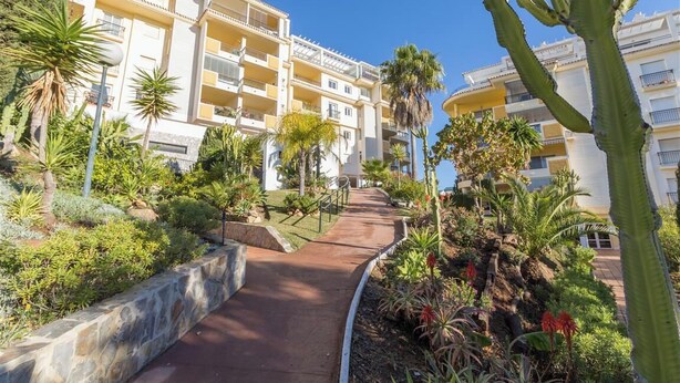 Un hotel con varios balcones, un sendero empedrado y una variedad de plantas tropicales.