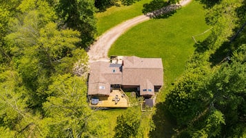 A single-story house with a deck, surrounded by dense greenery and a dirt path leading to it.