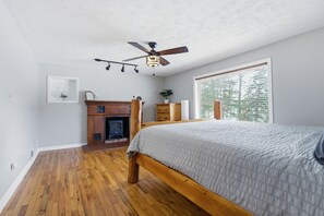 Ein Schlafzimmer mit einem hölzernen Bett, einem Deckenventilator, einem Kamin und einem Fenster mit Jalousien.
