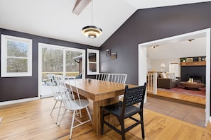 A dining area with a wooden table and chairs, large windows, and a view of the outdoors.