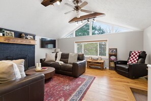 Ein Wohnzimmer mit Kamin, Ledersofas, Deckenventilator und großem Fenster.