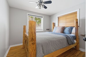 Une chambre avec un lit en bois, un ventilateur de plafond, une fenêtre avec des stores et une porte.