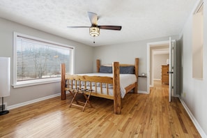 A bedroom with a wooden bed, a ceiling fan, a window with blinds, and a door leading to another room.