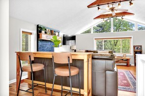 A modern kitchen with a bar area, wooden bar stools, and a ceiling fan. - Honeysuckle | Hocking Hills, Sauna, Hot Tub & Pets (Rockbridge)