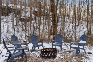 A snow-covered outdoor seating area with Adirondack chairs and a metal fire pit.