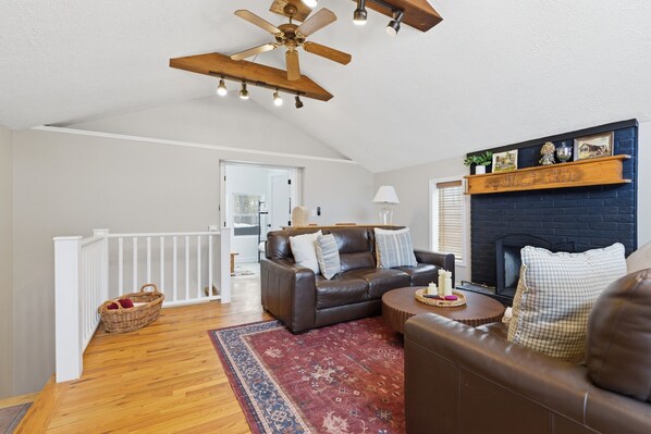 A spacious living room with a fireplace, a ceiling fan, and a wooden floor.