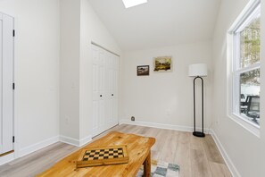 A room with a wooden bench, a chessboard, a floor lamp, and a window with a view of trees.