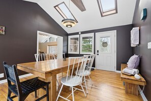 A dining area with a wooden table and chairs, a bench with towels, and a view through a door to a balcony.