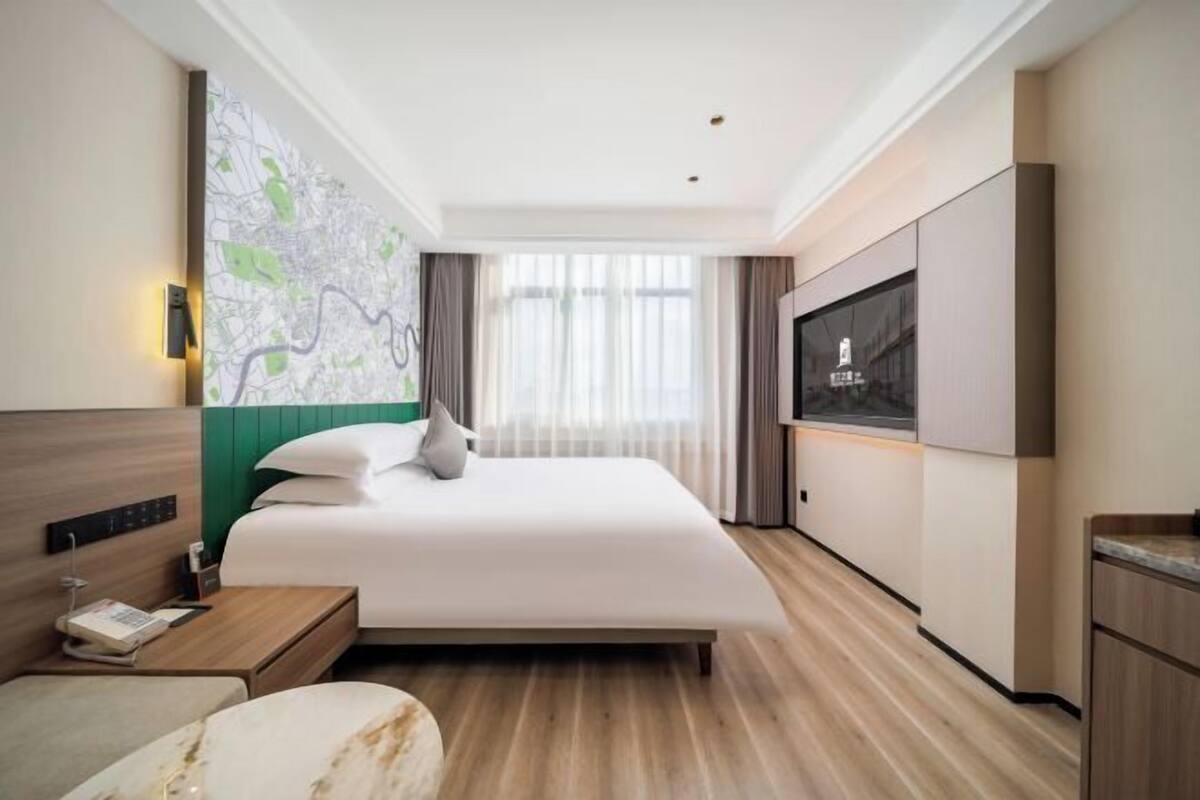 A hotel room with a large bed, a flat-screen TV, a wooden floor, and a map on the wall.