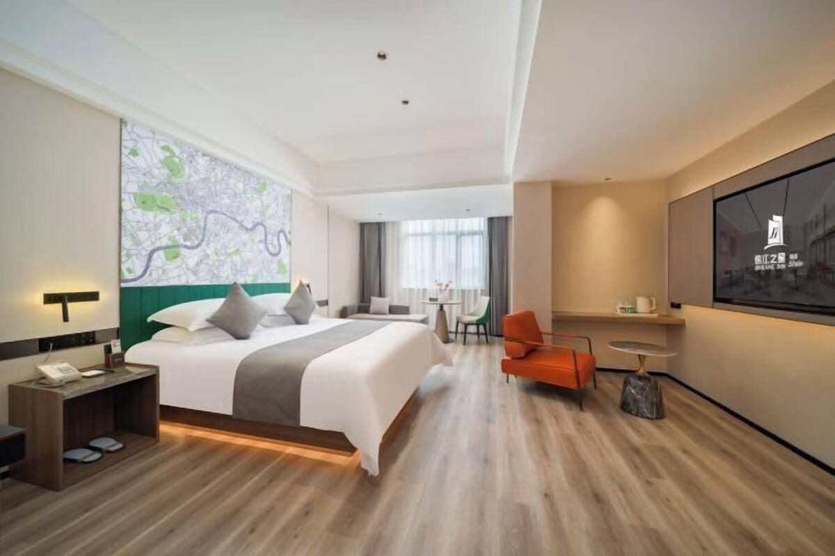 A hotel room with a large bed, a desk, a chair, a TV, and a map on the wall.