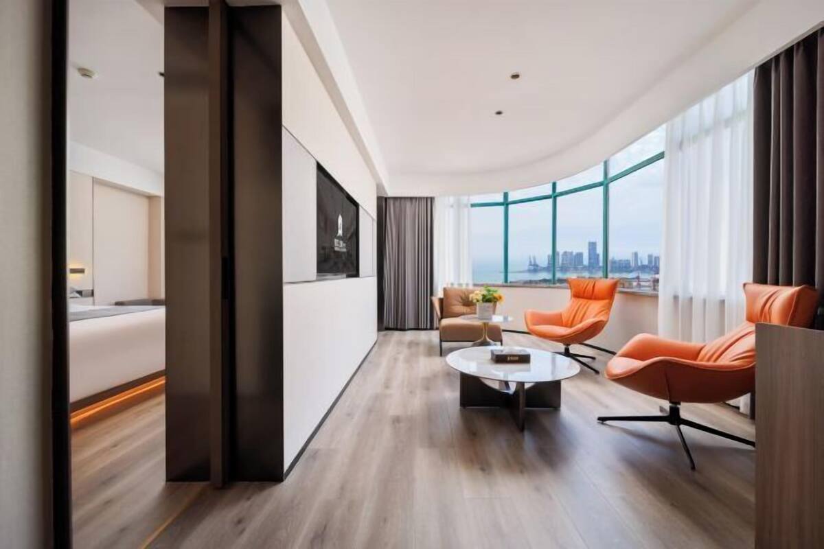 A modern hotel room with a city view, a large window, a sofa, and a coffee table.