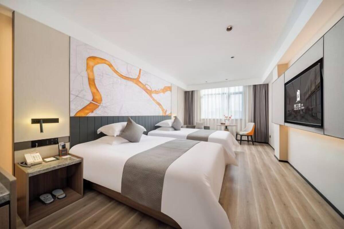 A modern hotel room with two beds, a large abstract artwork on the wall, a flat-screen TV, and a wooden floor.