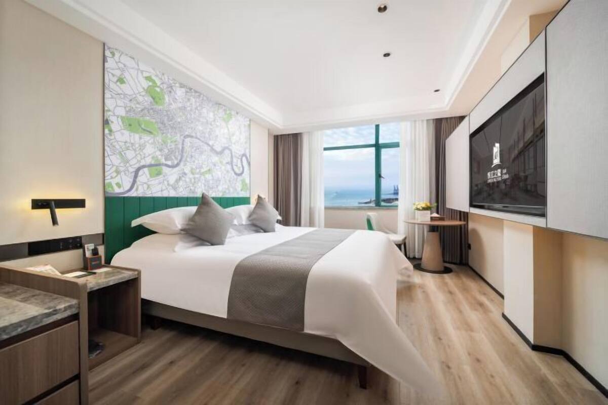 A modern hotel room with a large bed, a map on the wall, a TV, and a view of the sea.