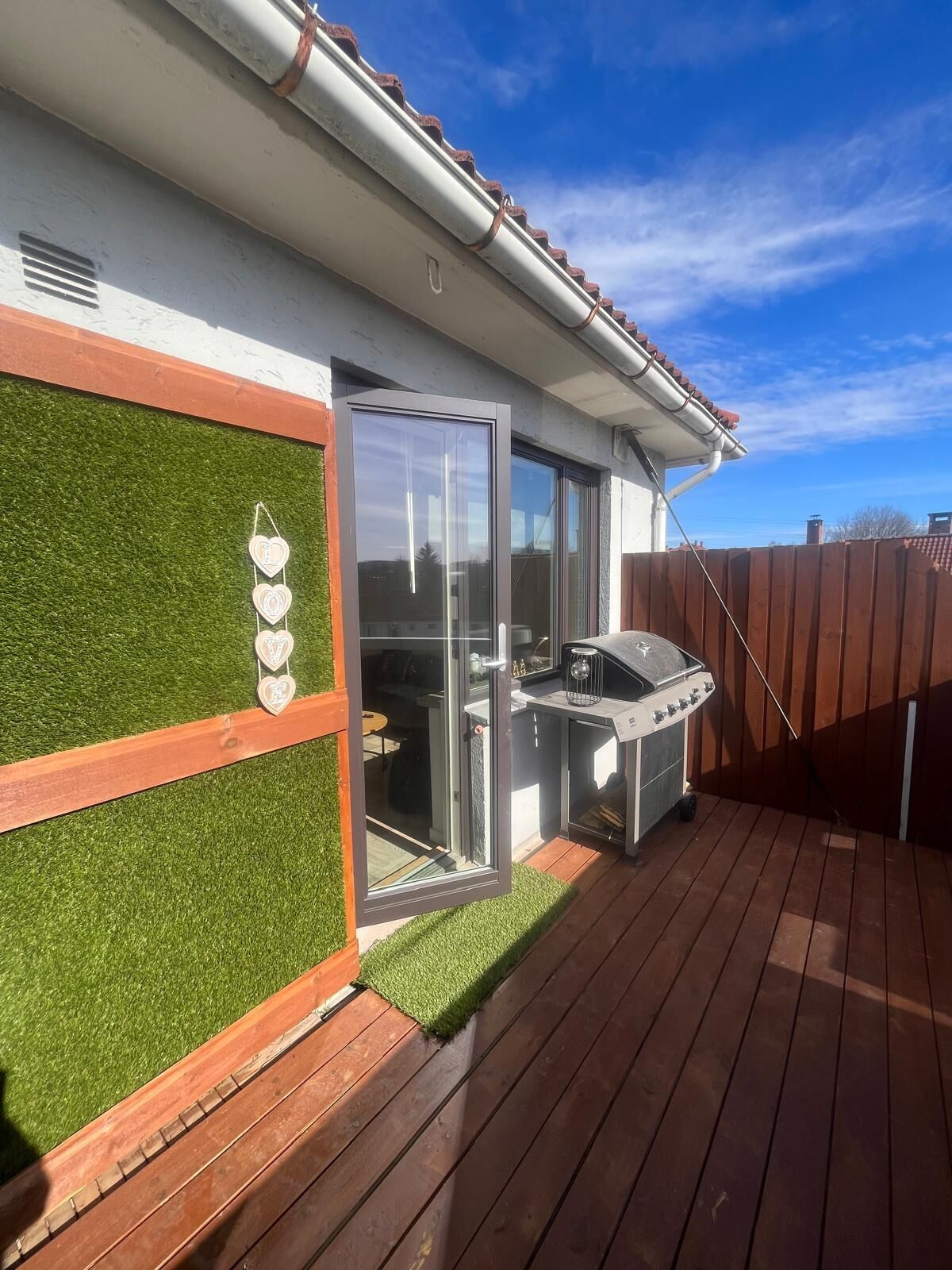 A deck with a barbecue grill, a glass door leading to a covered area, and a wooden fence.
