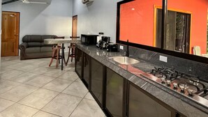 A modern kitchen with a central island, a built-in oven, and a large window with a red frame. - Ocean Breeze by Casa Pargo (Provincia de Puntarenas)