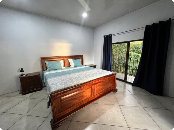 A bedroom with a wooden bed, a nightstand, a window with curtains, and a view of greenery outside. - Ocean Breeze by Casa Pargo (Provincia de Puntarenas)