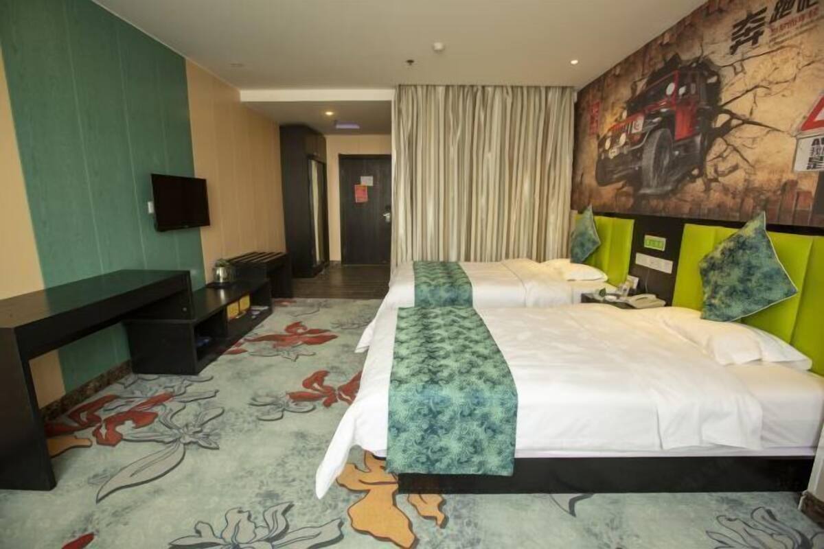 A hotel room with a bed, a desk, a television, and a mural on the wall.