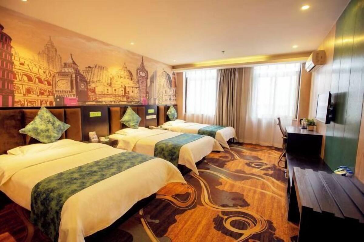 A hotel room with two beds, a desk, a television, and a mural of a cityscape.