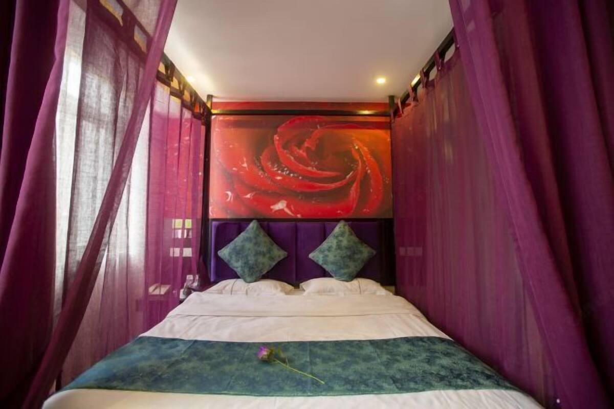 A bed with a headboard, curtains, and a wall with a red abstract design.