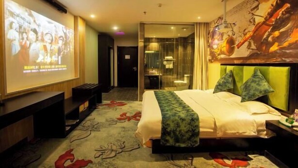 Una camera d'albergo con un letto, uno schermo televisivo, una scrivania e un bagno visibile attraverso una porta di vetro.