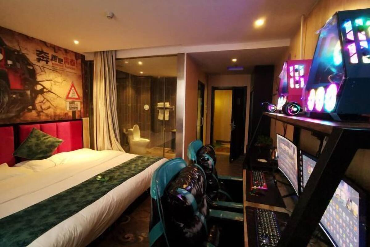 A hotel room with a bed, a desk with a computer, and a large screen.