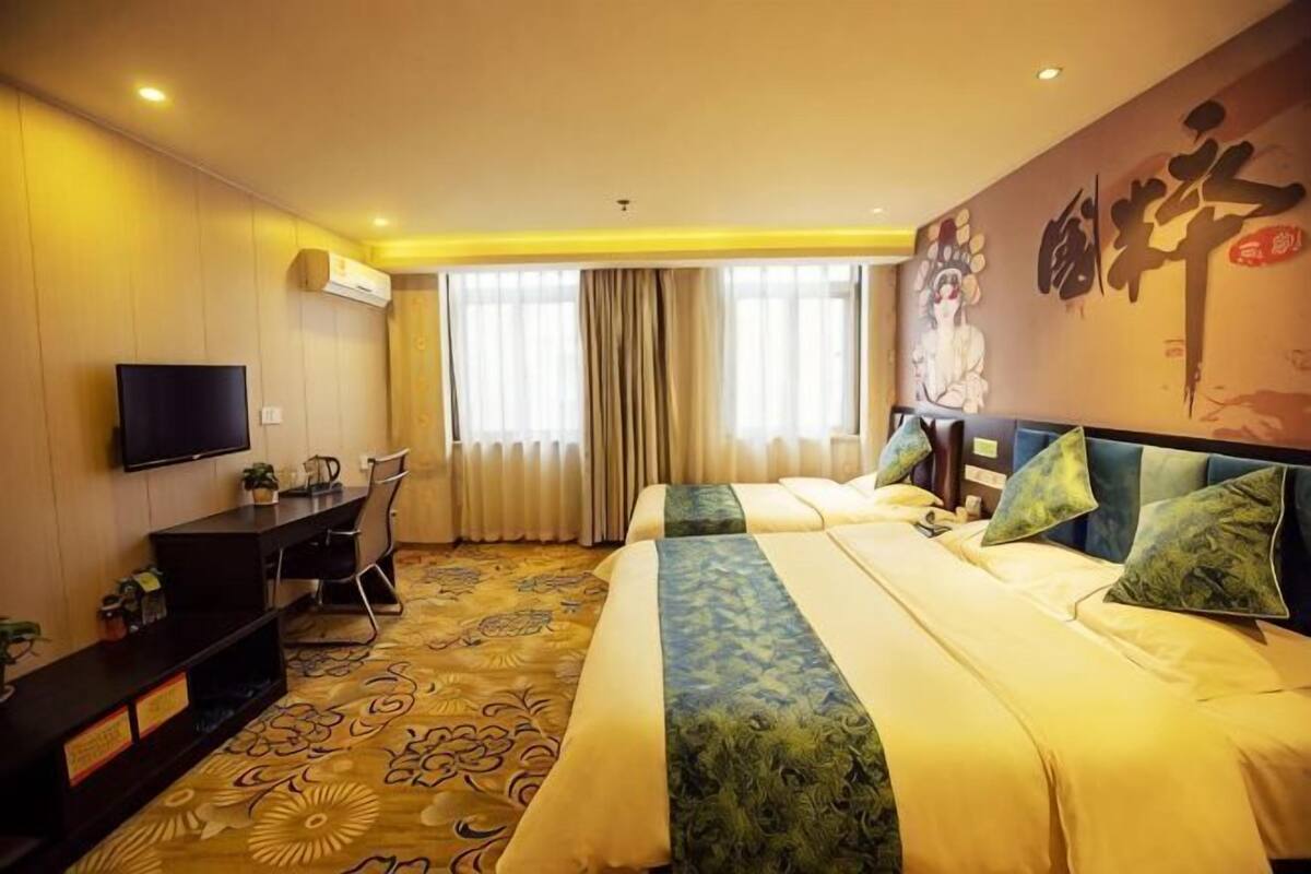 A hotel room with a bed, a desk, a chair, a TV, and a large window with curtains.