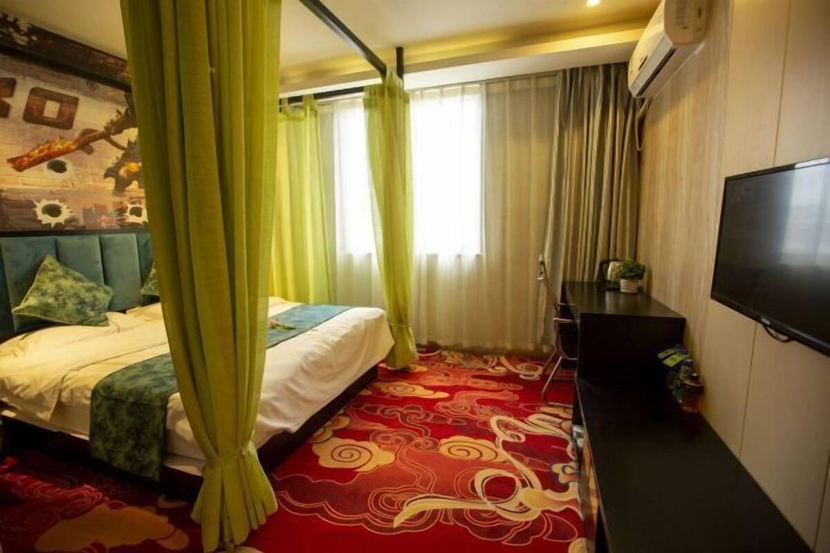 A hotel room with a bed, curtains, a TV, and a patterned carpet.