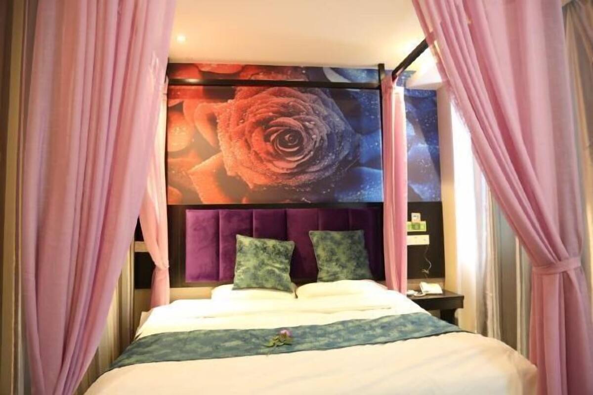 A bed with a headboard, two pillows, a bedside table, and a wall with a large floral artwork.