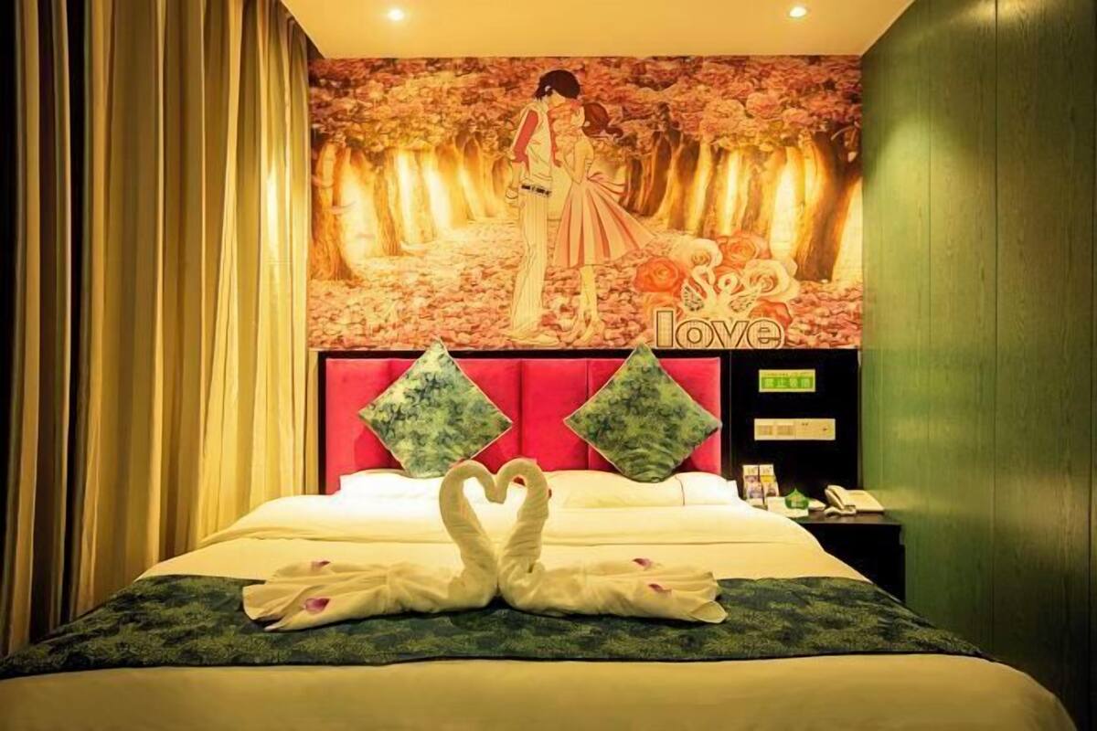 A hotel room with a bed, a red headboard, a wall mural, and a decorative swan towel arrangement.