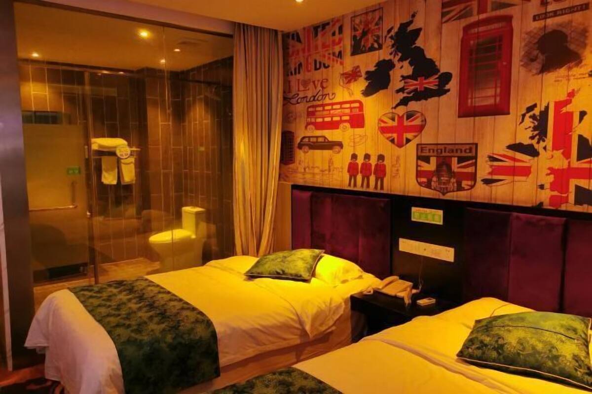 A hotel room with two beds, a glass shower enclosure, and a wall decorated with British-themed artwork.