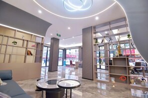 A modern lobby with a curved ceiling, a reception desk, seating area, and a glass partition with shelves. - Jin Jiang Hotel (Cangnan)