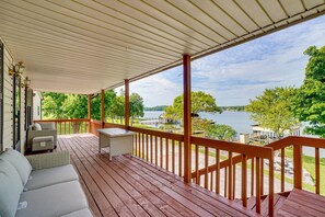 A covered deck with a view of a lake, featuring a wicker sofa and a small table. - Watts Bar Lake Retreat Private Dock, Boat Ramp & Stunning Views! (Spring City)