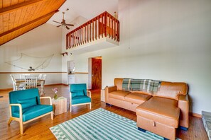 Amplia sala de estar con techo de madera, escalera estilo loft, una mesa de comedor con sillas, un sofá y una pequeña mesita con un jarrón.