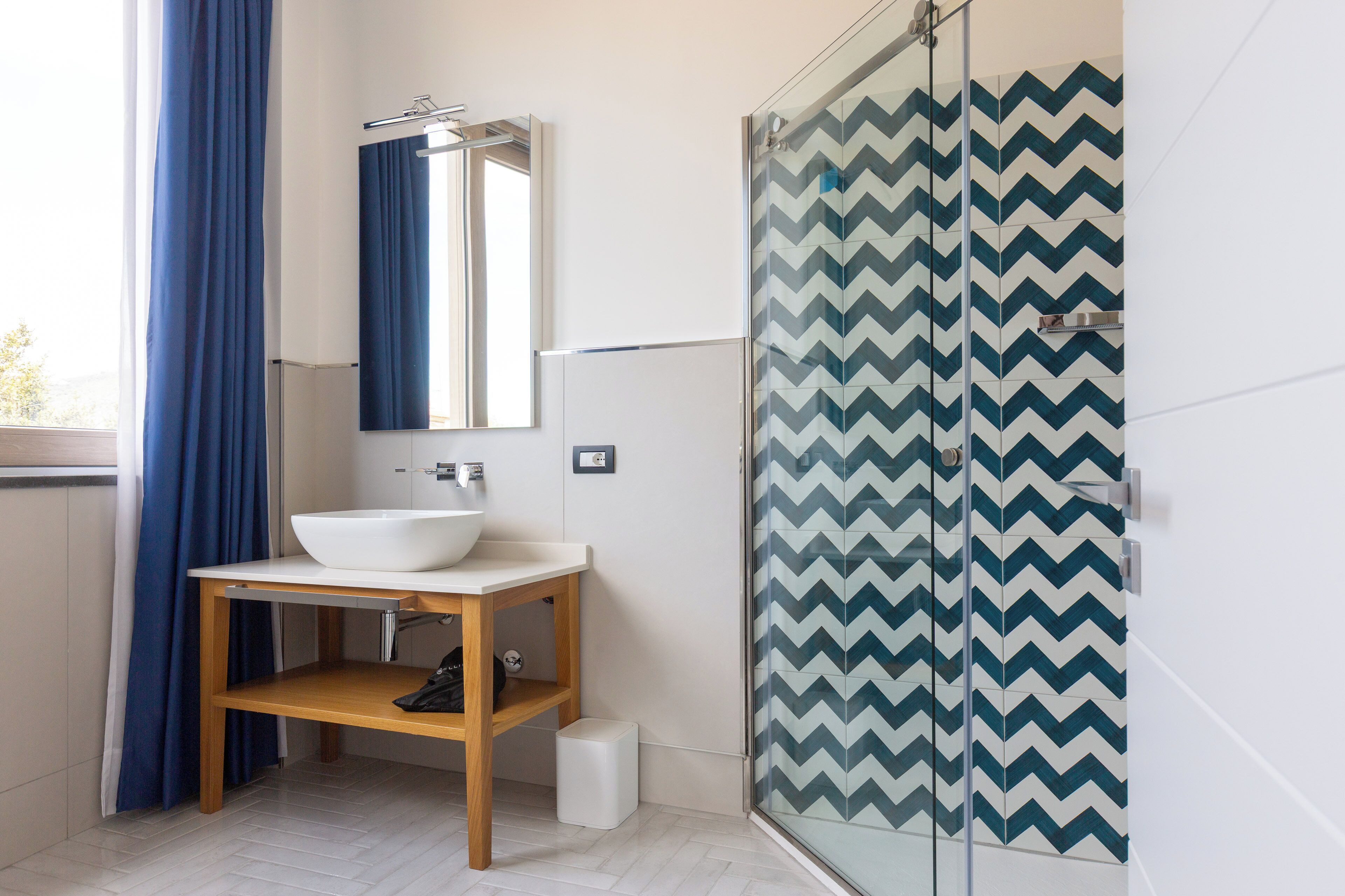 Ein modernes Badezimmer mit Waschbecken, Holzkommode und Duschkabine mit Zickzackfliesenmuster.