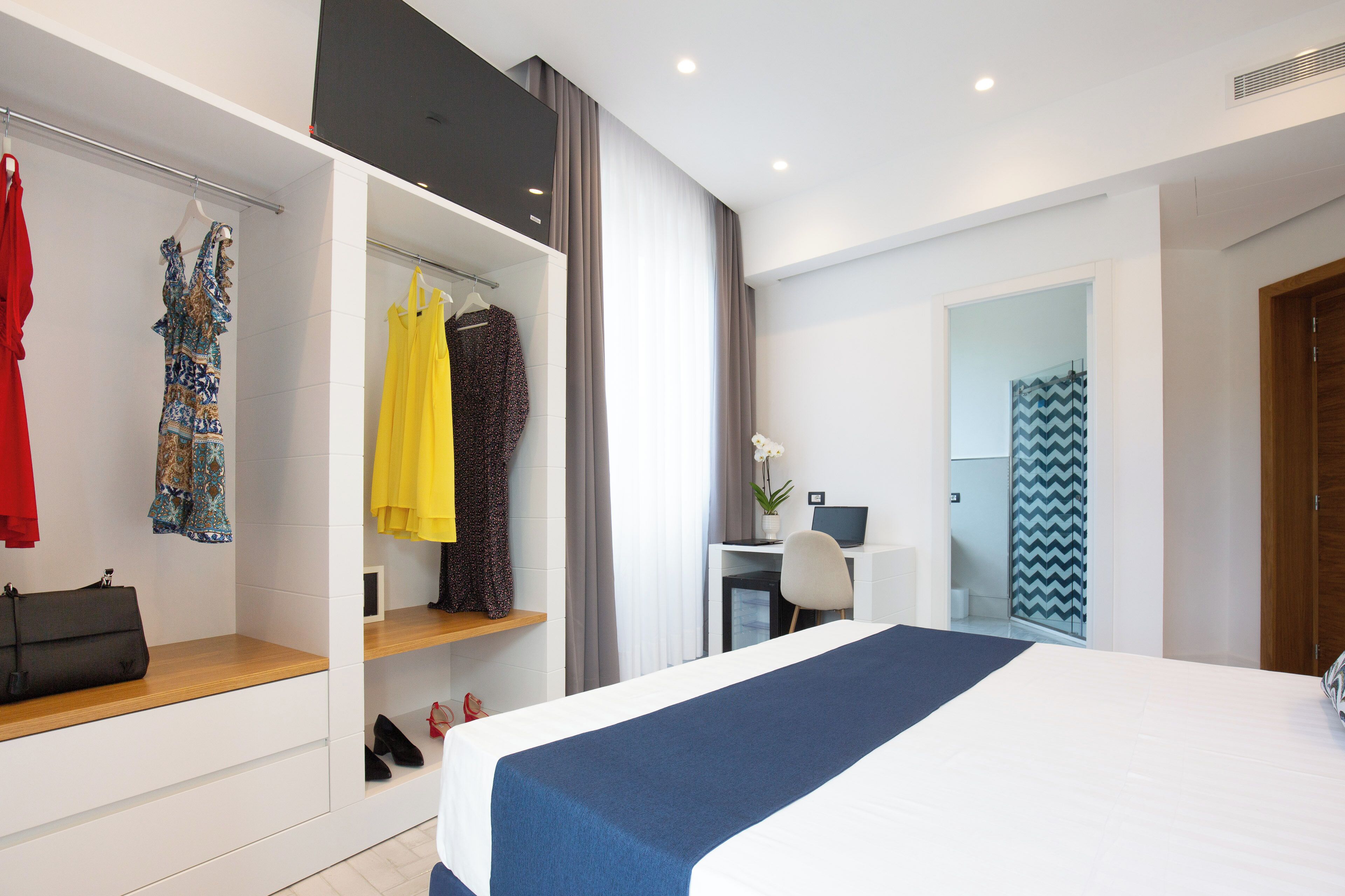 Quarto de hotel moderno com uma cama grande, uma escrivaninha e um guarda-roupa com roupas penduradas.