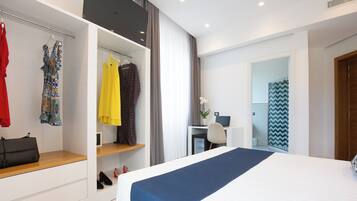Quarto de hotel moderno com uma cama grande, uma escrivaninha e um guarda-roupa com roupas penduradas.