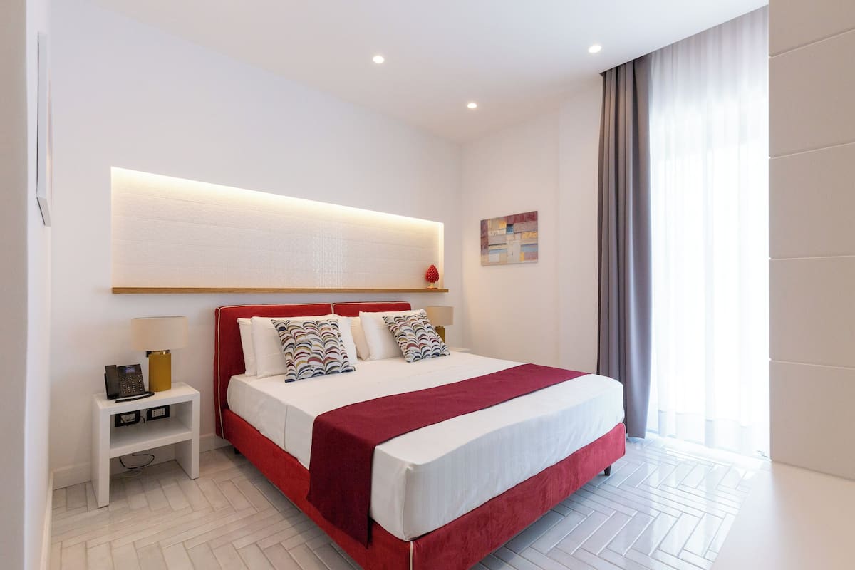 Ein modernes Hotelzimmer mit einem großen Bett, einem Nachttisch mit Lampe sowie einer Wandleuchte.