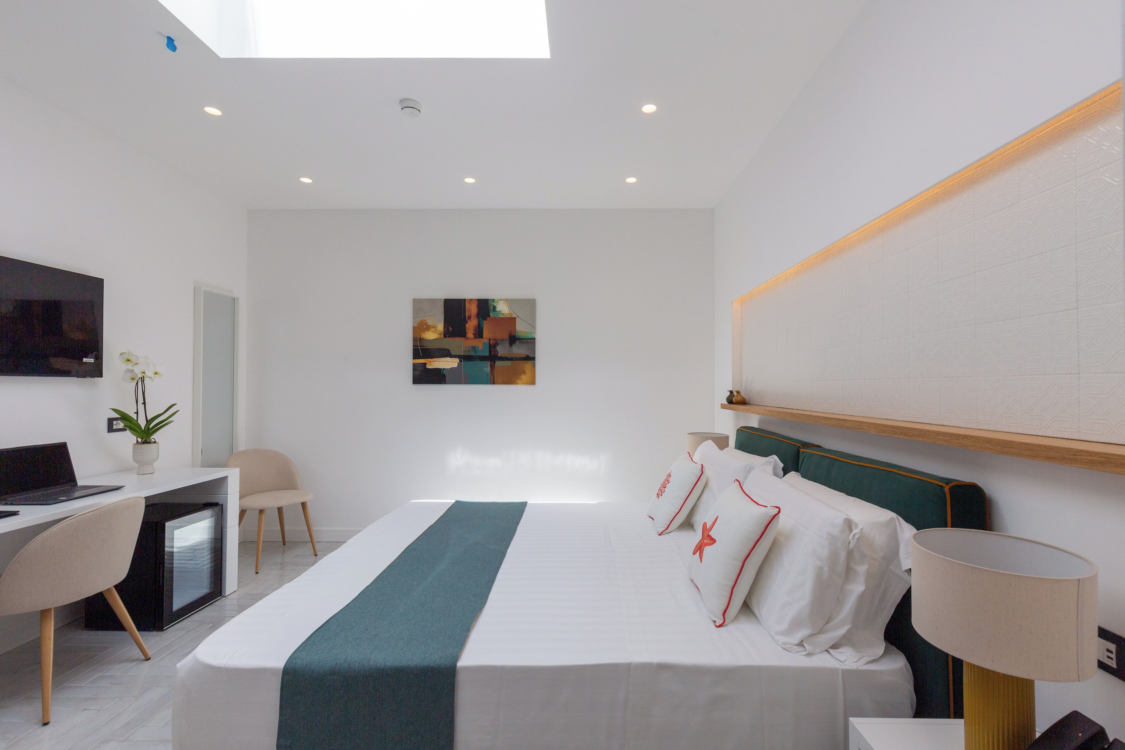 Una habitación de hotel moderna con cama, escritorio, silla y televisor en la pared.