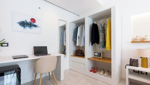 Ein modernes Zimmer mit Schreibtisch, Laptop, Stuhl und einem begehbaren Kleiderschrank mit Kleidung und Schuhen.